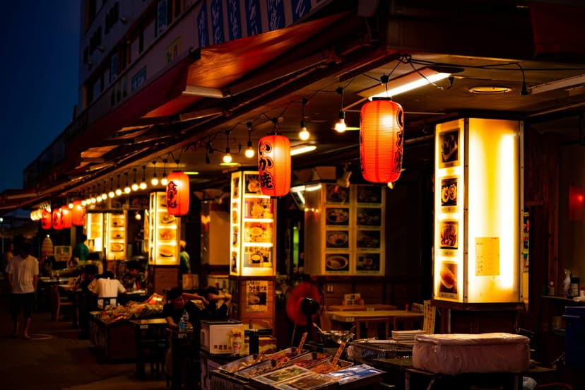 A row of small restaurants at dusk, lit by red lanterns