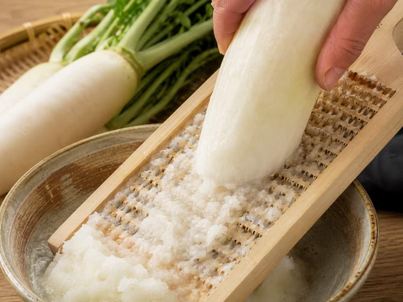 A traditional wooden Japanese daikon grater with a rough grating surface, resting over a bowl of grated daikon