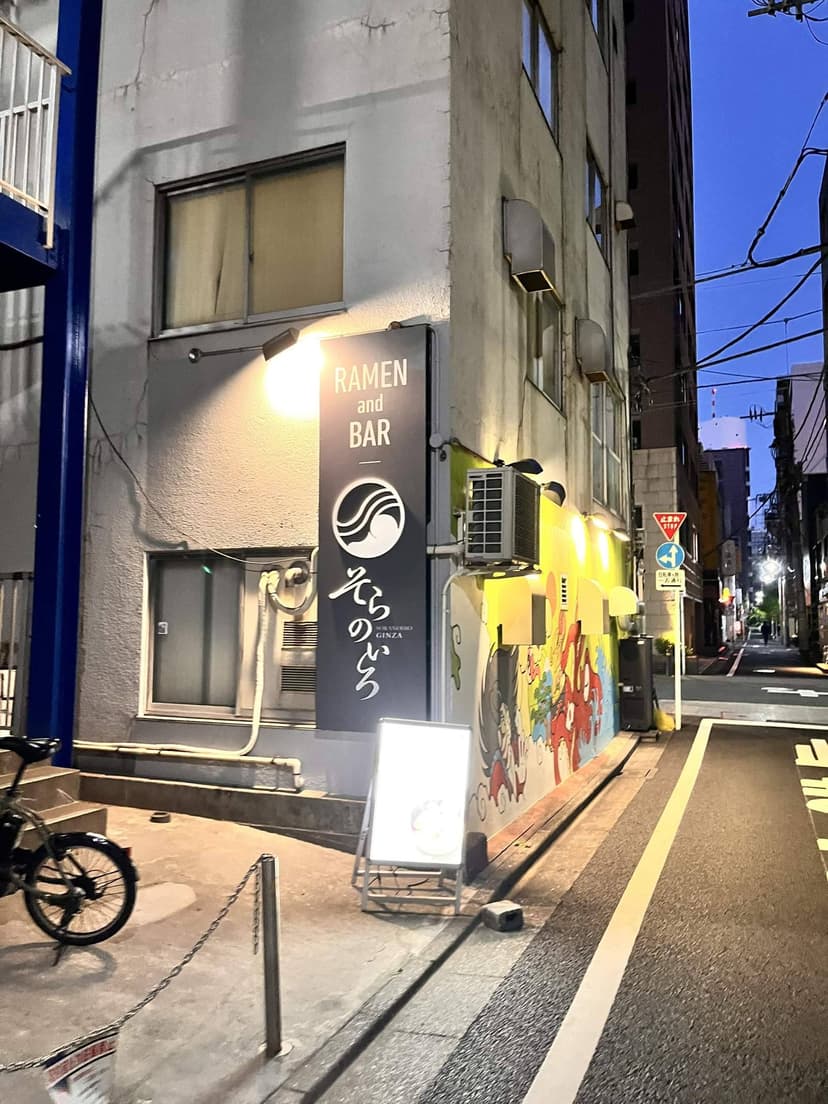 The Ginza flagship at dusk, with its RAMEN and BAR sign and the mural running down the side street